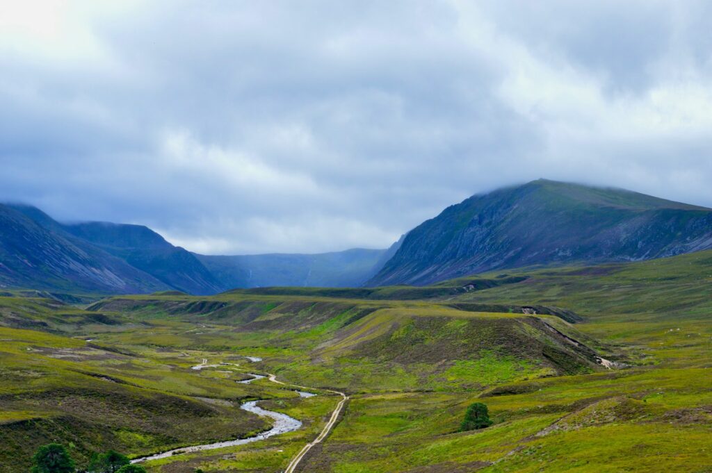 green grass field and mountain under white clouds in Cairngorms National Park