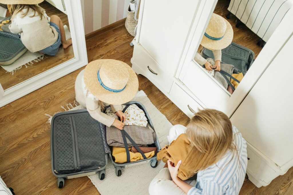 Child packing suitcase with help from mother, preparing for a summer trip.