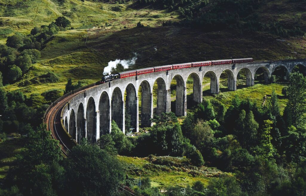 train on bridge surrounded with trees at daytime Glenfinnan Viaduct