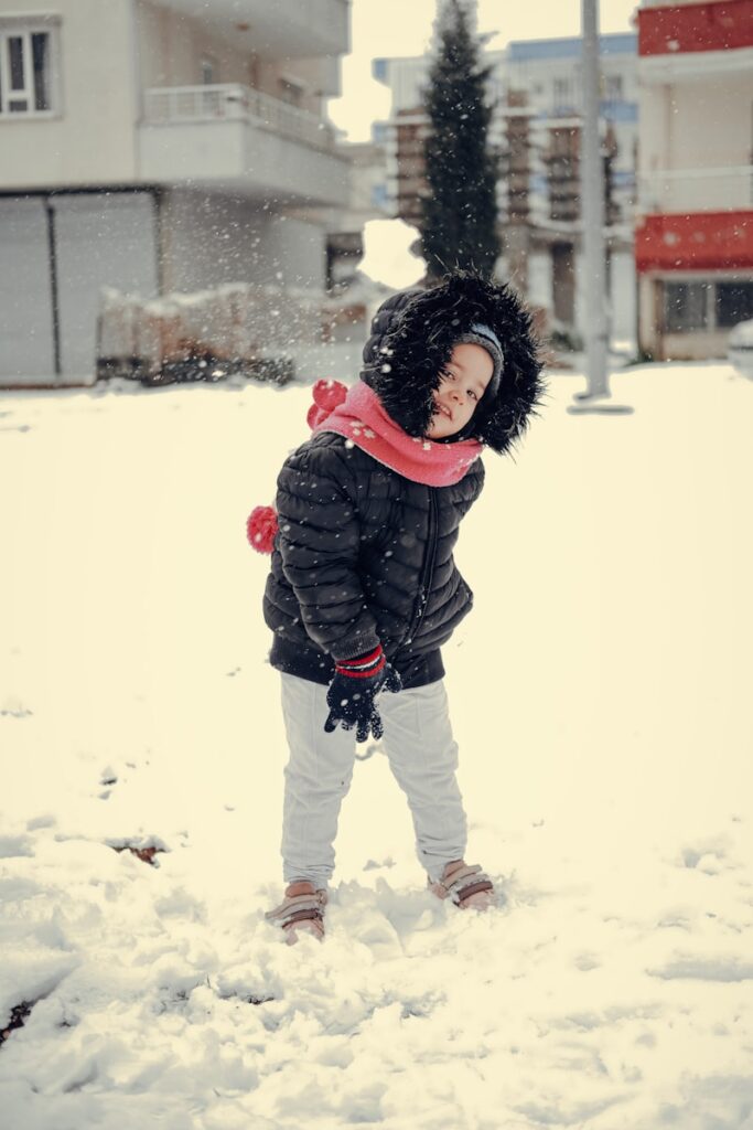 a little girl standing in the snow with a red scarf around her neck