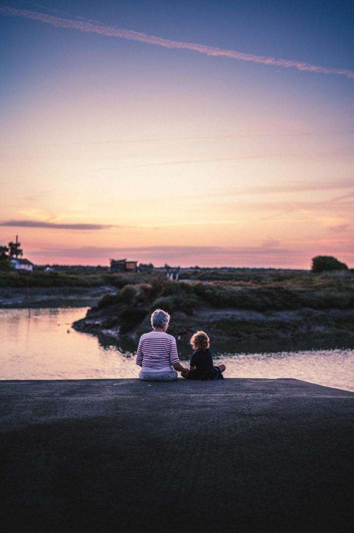 An adult and child sharing a tranquil moment by the water during a vibrant sunset in Arvert, France.